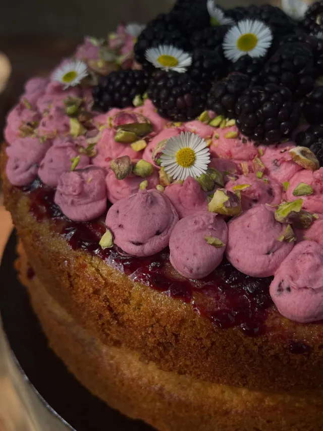 Cake topped with blackberry buttercream, fresh blackberries, pistachios and daisies