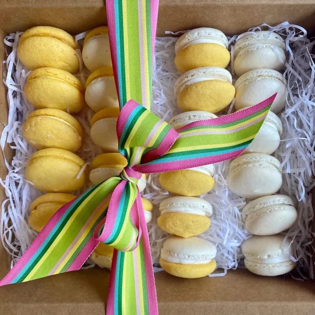 Box of yellow and white macarons tied with a striped ribbon