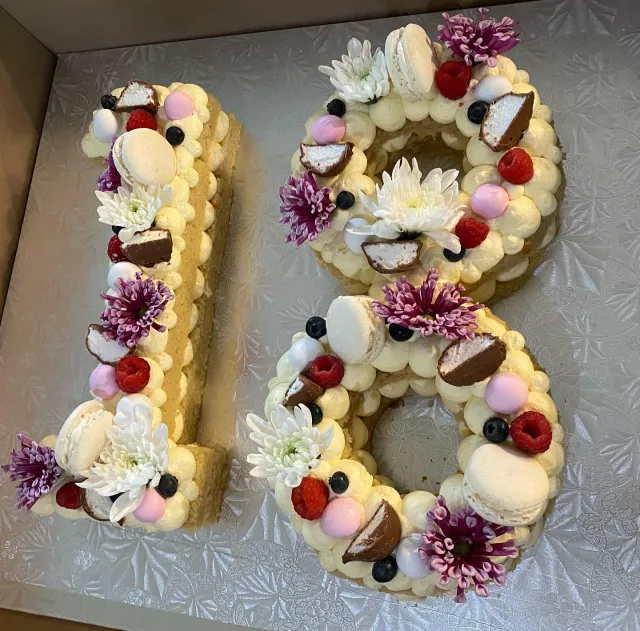Number 18 cake layered with cream, macarons, berries and flowers