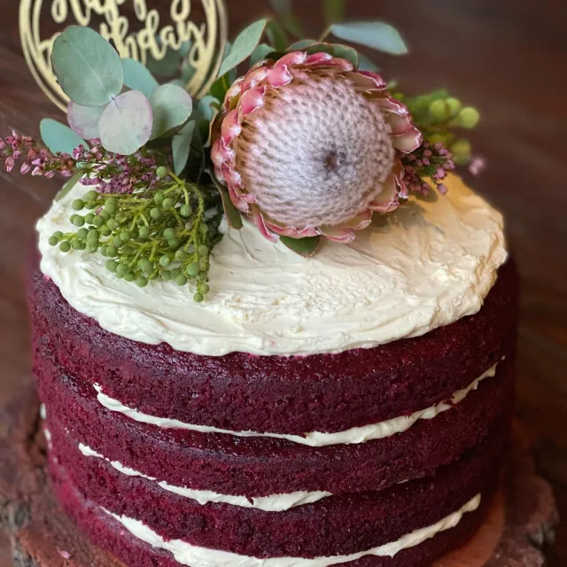 Red velvet naked cake topped with a pink protea and greenery