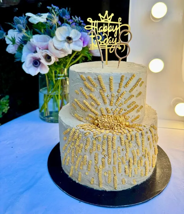 Two-tier white and gold birthday cake with a Happy Birthday topper